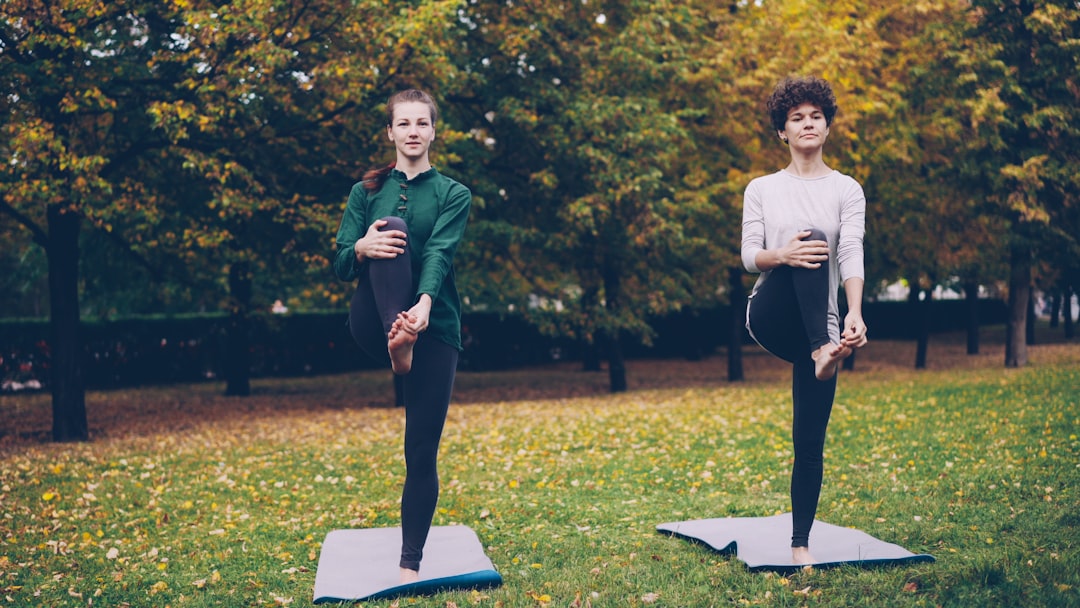 Offerings Couple of attractive girls are doing yoga in park practising balancing exercises standing on one leg during individual yoga practice with professional instructor.